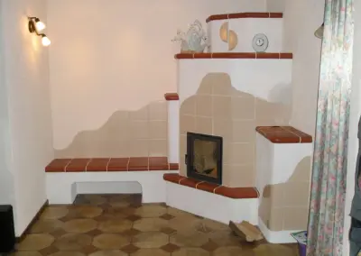 Klassischer Kachelofen mit heller Keramikverkleidung, Sichtfenster und umlaufender Sitzbank.