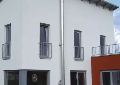 Außen montierter Edelstahlschornstein an einem modernen Wohnhaus, senkrecht bis über die Dachkante geführt.