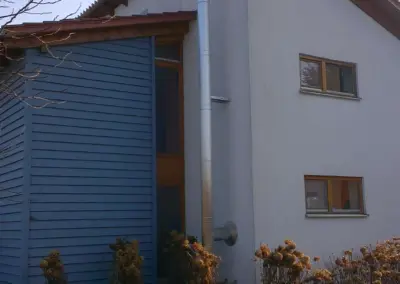 Nahaufnahme eines außen montierten Edelstahlschornsteins an der Giebelseite eines Wohnhauses.