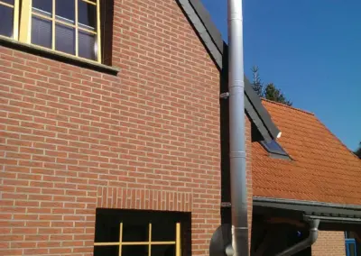 Gebürsteter Edelstahlschornstein an einer Klinkerfassade, außen montiert und bis über die Dachkante geführt.