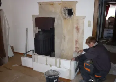 Kachelofen während des Aufbaus mit sichtbarem Heizeinsatz, heller Keramikverkleidung und Sitzbank.