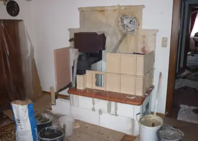 Kachelofen mit heller Keramikverkleidung während des Aufbaus mit sichtbarem Heizeinsatz und Sitzbank.