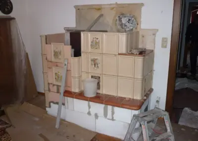 Kachelofen mit heller Keramikverkleidung während des Aufbaus mit sichtbaren Bauteilen und noch offener Unterkonstruktion.