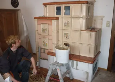 Kachelofen mit heller Keramikverkleidung während der Montage mit sichtbaren Bauteilen und Arbeitsmaterialien.