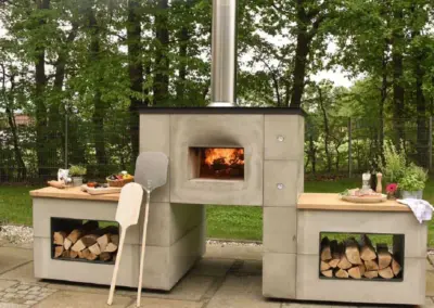 GRANNUS Außenbackofen mit zentraler Backkammer, seitlichen Ablagen und integrierten Holzfächern im Garten.