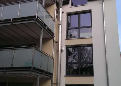 Außen montierter Edelstahlschornstein an einem mehrgeschossigen Wohngebäude mit Balkonen.