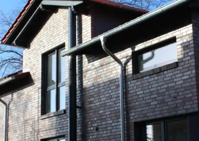Farbbeschichteter Außenschornstein aus Edelstahl an einem Wohnhaus, fotografiert aus seitlicher Perspektive.