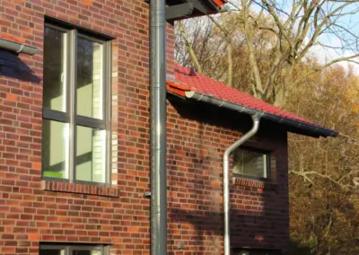 Farbbeschichteter Außenschornstein aus Edelstahl an einem Wohnhaus mit roter Klinkerfassade.