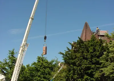 AKM Masche montiert mit einem Kran einen gemauerten Schornstein auf ein Dach.