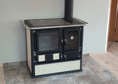 La Nordica Holzbackofen: Klassischer Holzherd mit Kochfeld, Backofen, schwarzem Rauchrohr und heller Front.Bodenbereich.