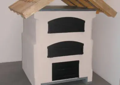 Outdoor-Backofen mit verputztem Korpus, drei Öffnungen und schützendem Holzdach für den Außenbereich.