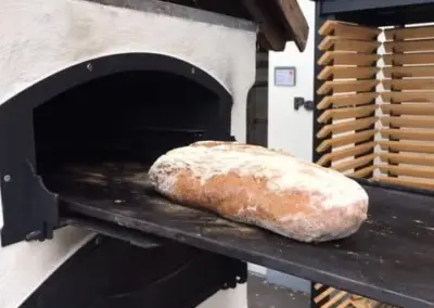 Outdoor-Backofen mit offener Backkammer und frisch gebackenem Brot auf einem ausziehbarem Backblech.