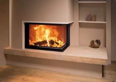 BRUNNER Eckkamin mit großer Eckscheibe, heller Verkleidung und integrierter Ablagefläche im Wohnraum.