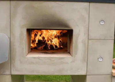 Grannus Outdoor Holzbackofen mit offenem Feuerraum, Holzfeuer und zwei seitlich integrierten Temperaturanzeigen.
