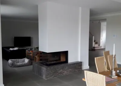 Moderner Panoramakamin mit Naturstein-Feuertisch, Eckverglasung und breiter Sicht auf den Feuerraum im offenen Wohnbereich.