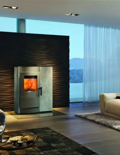 RIKA INDUO Kombiofen mit Specksteinverkleidung, großer Sichtscheibe und sichtbarem Feuer im modernen Wohnraum.