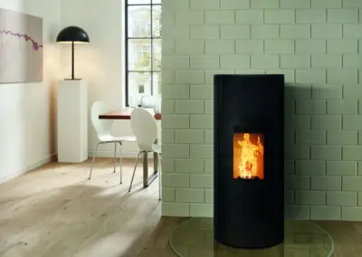 RIKA CORSO Pelletofen mit schwarzem Korpus, hoher Sichtscheibe und sichtbarem Feuer im Wohnbereich.