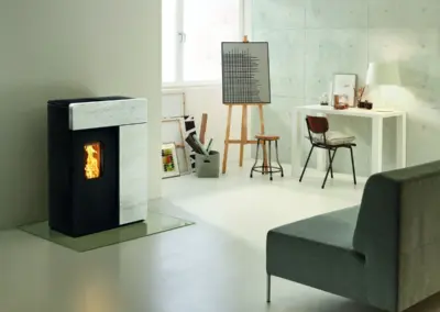 RIKA DOMO Pelletofen mit heller Steinverkleidung, schwarzer Front und sichtbarem Feuer im Wohnraum.